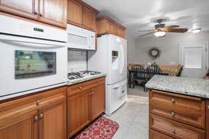 Kitchen with ceiling fan, light tile patterned floors, white appliances, tasteful backsplash, and light stone countertops