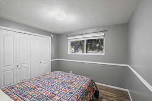 Bedroom with a textured ceiling, a closet, and dark hardwood / wood-style flooring