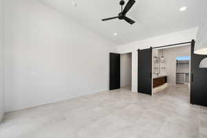 Unfurnished bedroom featuring a spacious closet, ceiling fan, a barn door, and vaulted ceiling