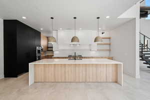 Kitchen featuring stainless steel double oven, decorative light fixtures, sink, an island with sink, and a textured ceiling