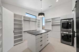 Spacious closet featuring stacked washer and clothes dryer and light carpet