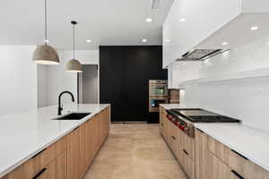 Kitchen featuring pendant lighting, sink, wall chimney range hood, appliances with stainless steel finishes, and light stone countertops