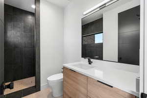 Bathroom featuring tile patterned floors, toilet, tiled shower, and vanity