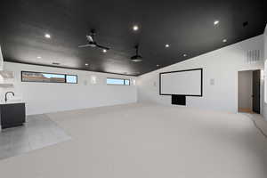 Carpeted cinema room with lofted ceiling, ceiling fan, sink, and a textured ceiling