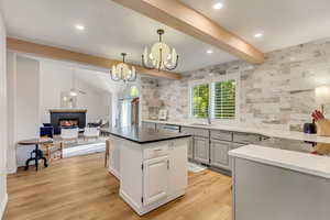 Kitchen with sink, hanging light fixtures, a stone fireplace, and light hardwood / wood-style flooring