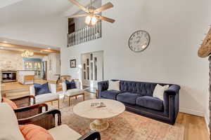 Living room with ceiling fan with notable chandelier, high vaulted ceiling, and hardwood / wood-style floors