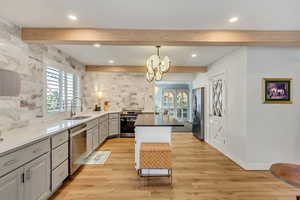 Kitchen featuring beamed ceiling, light wood-type flooring, gray cabinetry, sink, and appliances with stainless steel finishes