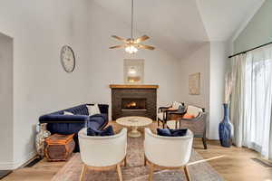 Sitting room with ceiling fan, light hardwood / wood-style floors, high vaulted ceiling, and a stone fireplace