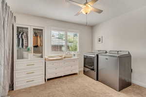 Laundry room featuring independent washer and dryer, light colored carpet, and ceiling fan