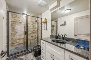 Full bath with a shower stall, a textured ceiling, toilet, and vanity