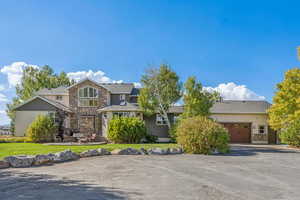 View of front facade with a garage, stone siding, roof with shingles, and a front lawn