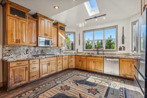 Kitchen with a skylight, appliances with stainless steel finishes, backsplash, light stone countertops, and glass insert cabinets