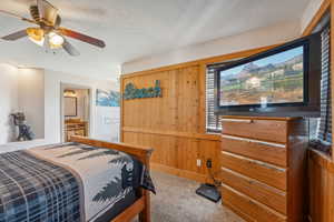 Bedroom with carpet floors, wood walls, ensuite bath, and ceiling fan