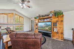 Living area featuring ceiling fan, carpet, baseboards, and vaulted ceiling