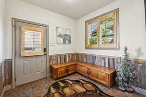 Doorway to outside featuring stone finish flooring, wainscoting, and wood walls