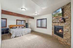 Carpeted bedroom featuring baseboards, a stone fireplace, a textured ceiling, and beamed ceiling