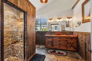 Bathroom featuring wainscoting, lofted ceiling, wood walls, a shower stall, and a sink