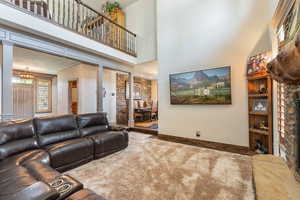 Living area featuring decorative columns, baseboards, a high ceiling, crown molding, and carpet flooring