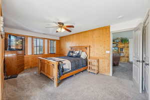 Carpeted bedroom featuring a ceiling fan and wooden walls