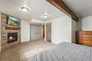 Carpeted bedroom featuring beamed ceiling, a stone fireplace, and baseboards