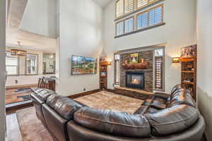 Living room with a fireplace, wood finished floors, a towering ceiling, and baseboards
