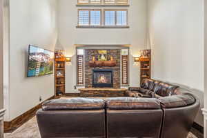 Living area with baseboards, a stone fireplace, a towering ceiling, and wood finished floors