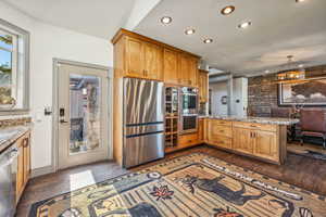 Kitchen with appliances with stainless steel finishes, light stone counters, dark wood-type flooring, a peninsula, and recessed lighting