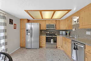 Kitchen with stainless steel appliances, light brown cabinets, sink, and a textured ceiling