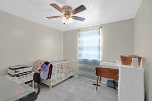 Carpeted bedroom with ceiling fan, a crib, and a textured ceiling