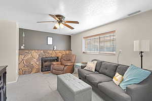 Living room with a fireplace, ceiling fan, carpet floors, and a textured ceiling