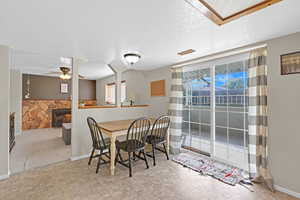 Dining space with a stone fireplace, light colored carpet, a textured ceiling, and ceiling fan