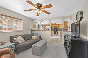 Living room featuring ceiling fan, light colored carpet, and a textured ceiling