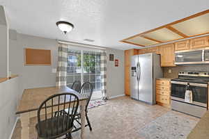 Kitchen featuring light brown cabinetry, a textured ceiling, stainless steel appliances, and backsplash