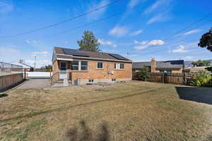 Rear view of house with a patio, a lawn, and solar panels