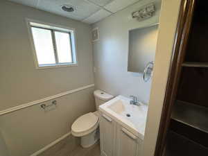 Bathroom featuring a paneled ceiling, vanity, hardwood / wood-style floors, and toilet