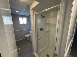 Bathroom featuring wood-type flooring, a drop ceiling, toilet, and an enclosed shower