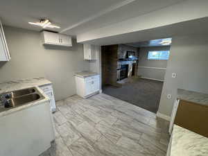 Kitchen with light colored carpet, a fireplace, sink, and white cabinetry