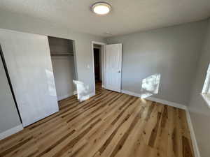 Unfurnished bedroom with light wood-type flooring, a closet, and a textured ceiling