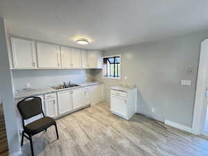 Kitchen featuring light wood-type flooring, white cabinets, sink, and light stone counters