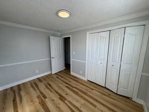 Unfurnished bedroom with ornamental molding, a textured ceiling, a closet, and light hardwood / wood-style flooring