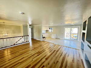 Unfurnished living room with a textured ceiling, ornate columns, an inviting chandelier, and light hardwood / wood-style flooring