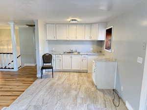 Kitchen with light hardwood / wood-style flooring, sink, decorative columns, ornamental molding, and white cabinetry