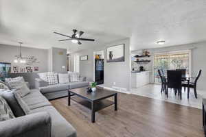 Living room featuring ceiling fan with notable chandelier, light hardwood / wood-style flooring, and a textured ceiling