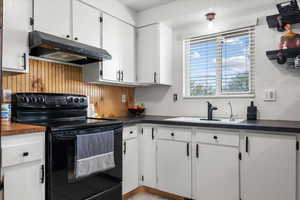 Kitchen featuring black electric range, sink, and white cabinetry