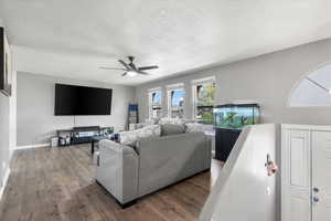 Living room with dark wood-type flooring, a textured ceiling, and ceiling fan