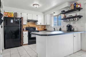 Kitchen with kitchen peninsula, black appliances, a textured ceiling, and white cabinetry