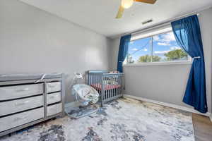 Bedroom with hardwood / wood-style floors, ceiling fan, a crib, and a textured ceiling