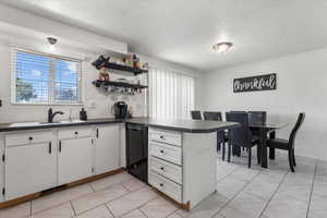 Kitchen with sink, dishwasher, kitchen peninsula, white cabinets, and a textured ceiling