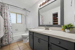 Full bathroom featuring vanity, a textured ceiling, shower / bath combo with shower curtain, tile patterned floors, and toilet