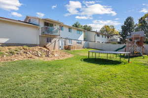 View of yard with a trampoline, a balcony, and a playground